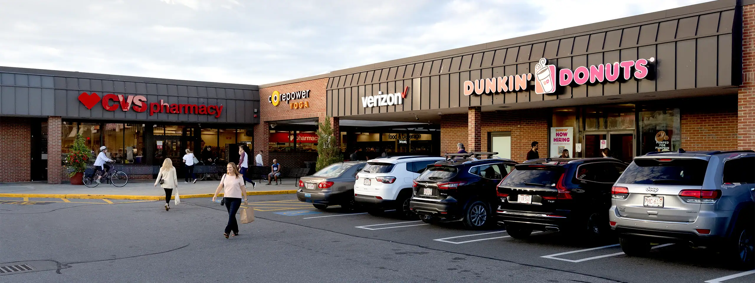 Shopping plaza with CVS, Dunkin' Donuts, Verizon stores and parked cars.
