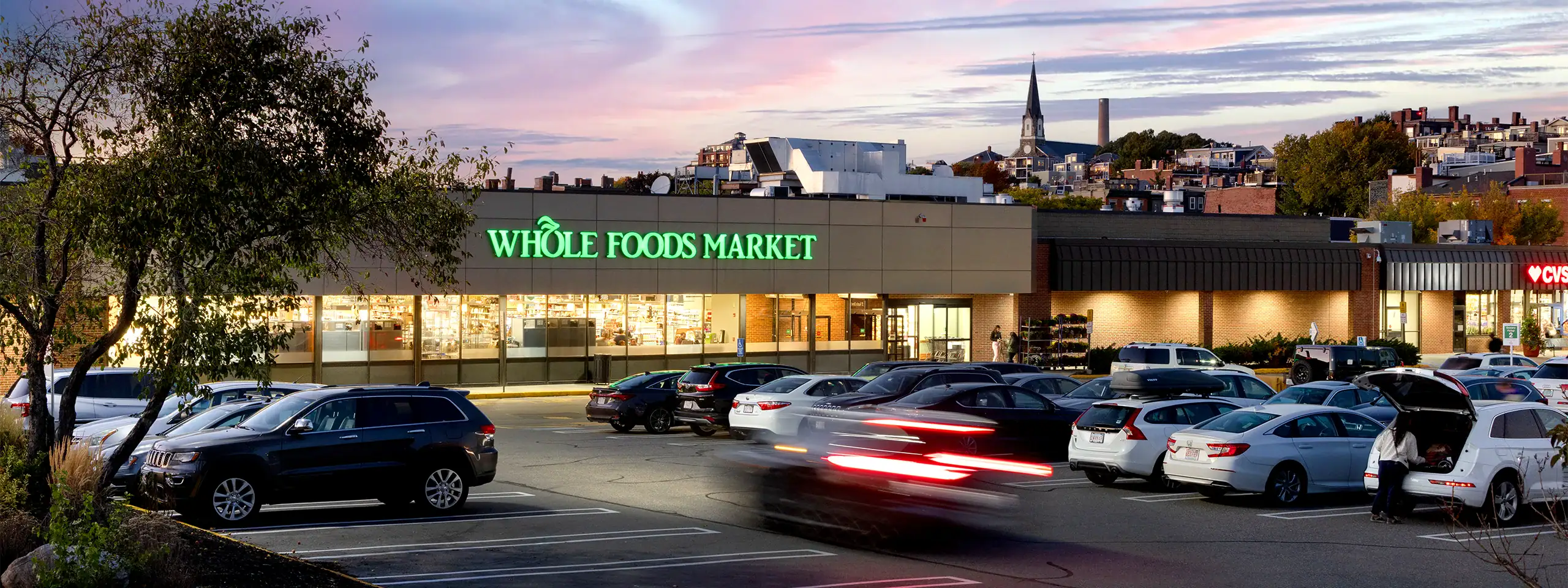 Whole Foods Market storefront with parking lot and city skyline in background.