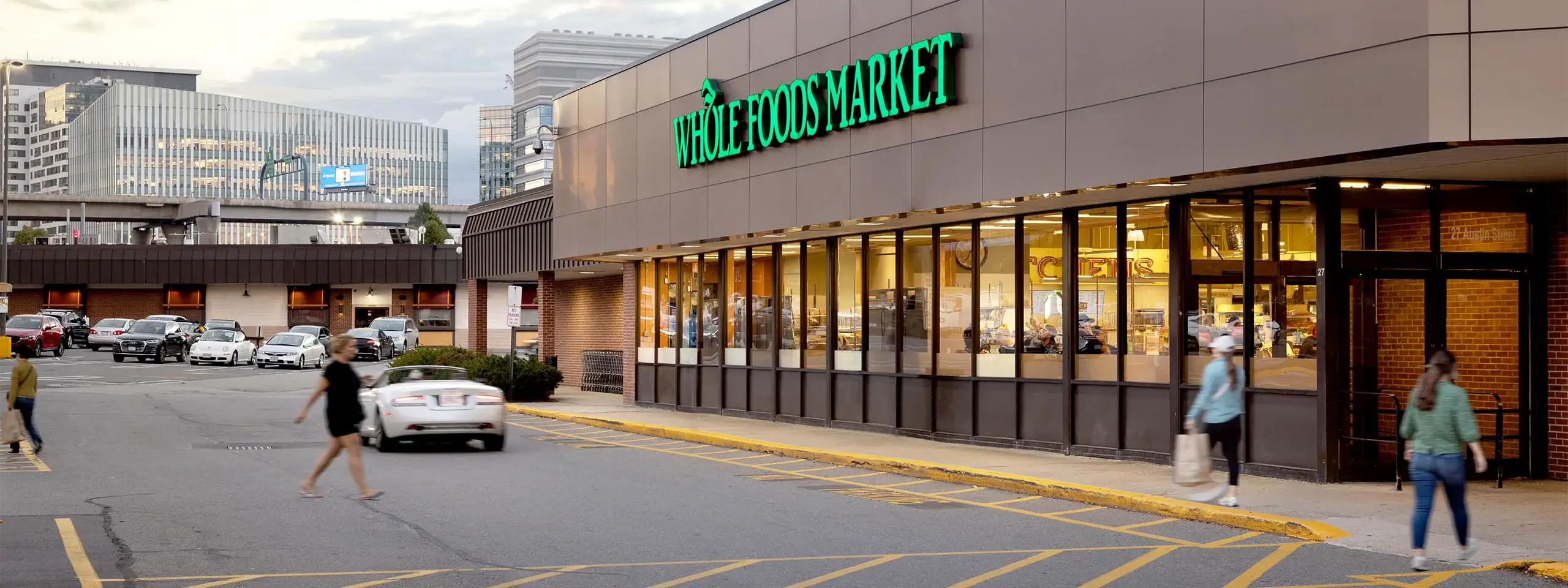 People walking past a Whole Foods Market in an urban shopping area.