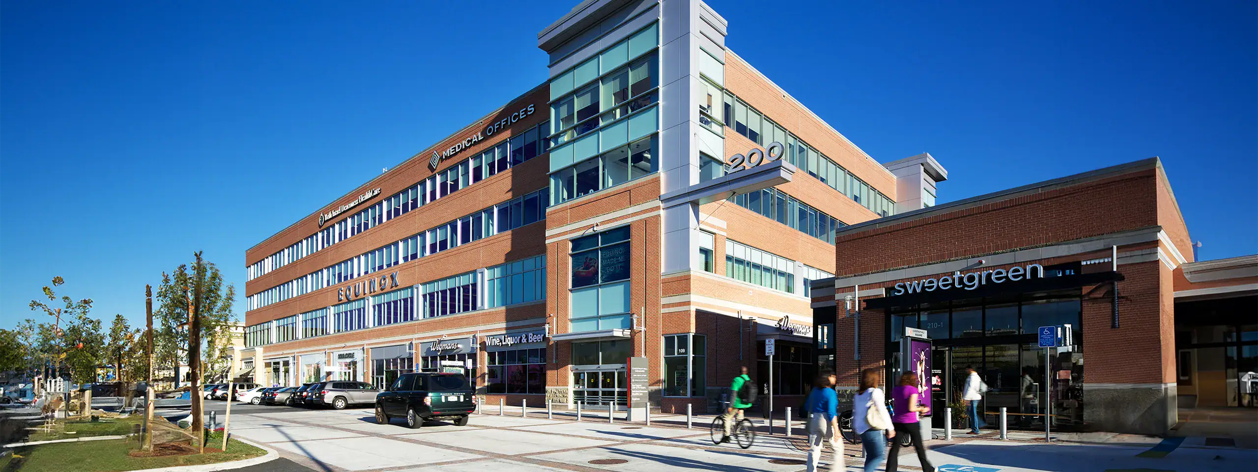Modern multi-story commercial building with retail stores and parking lot.