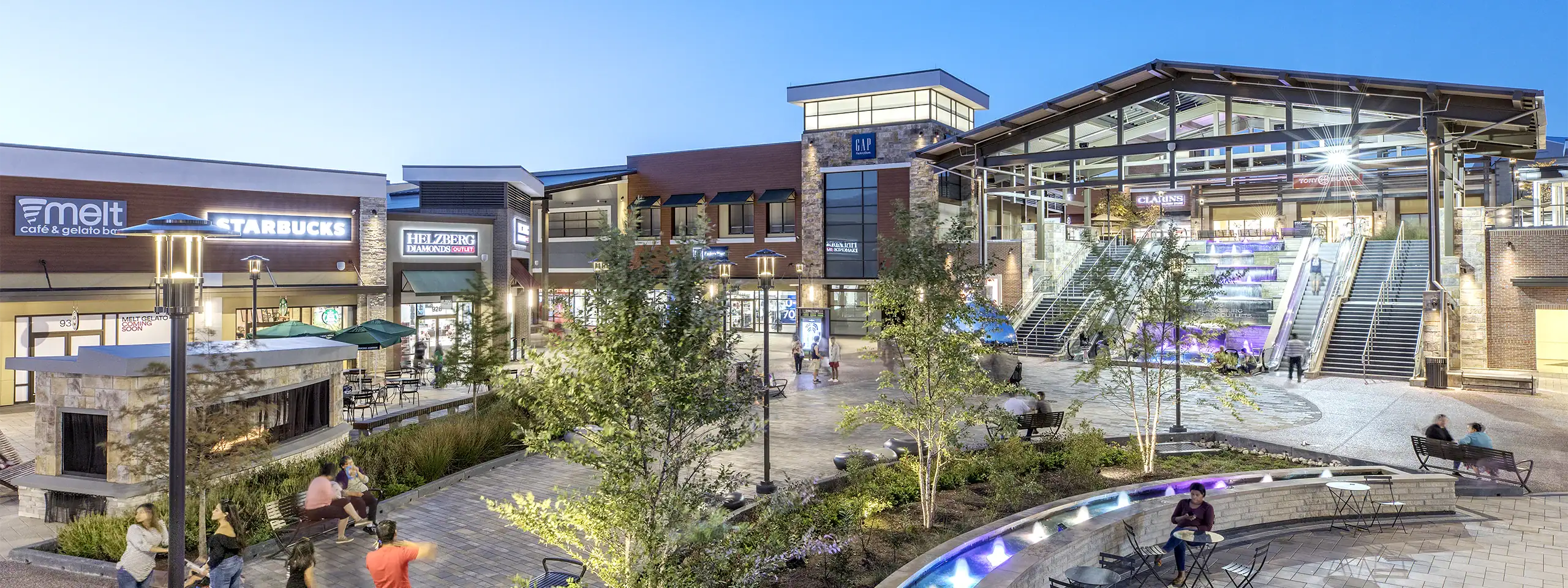 Outdoor shopping center with stores, trees, and seating areas at night.