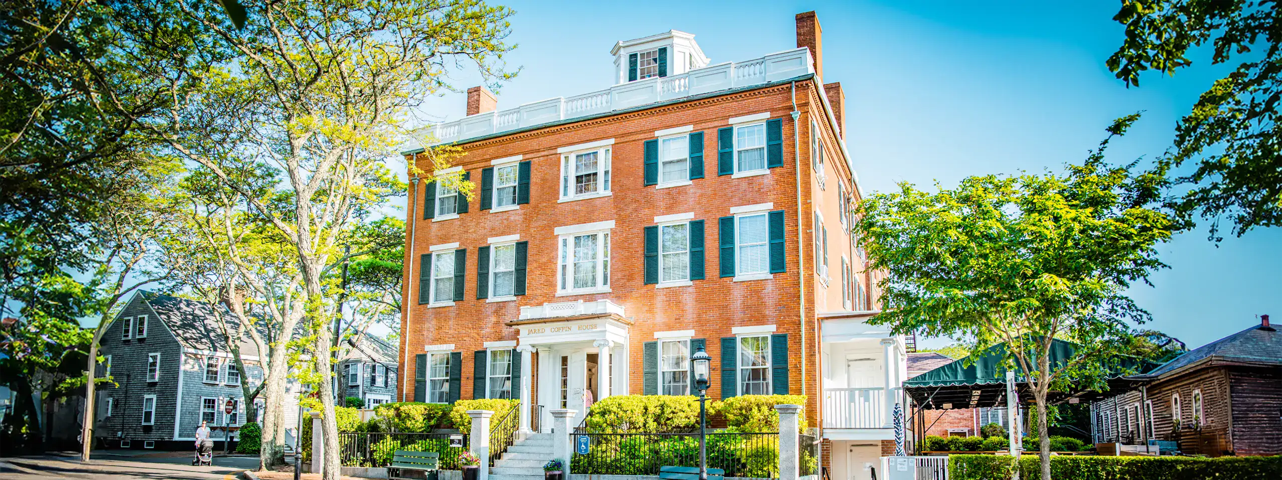Historic brick building with white trim and black shutters, surrounded by trees.