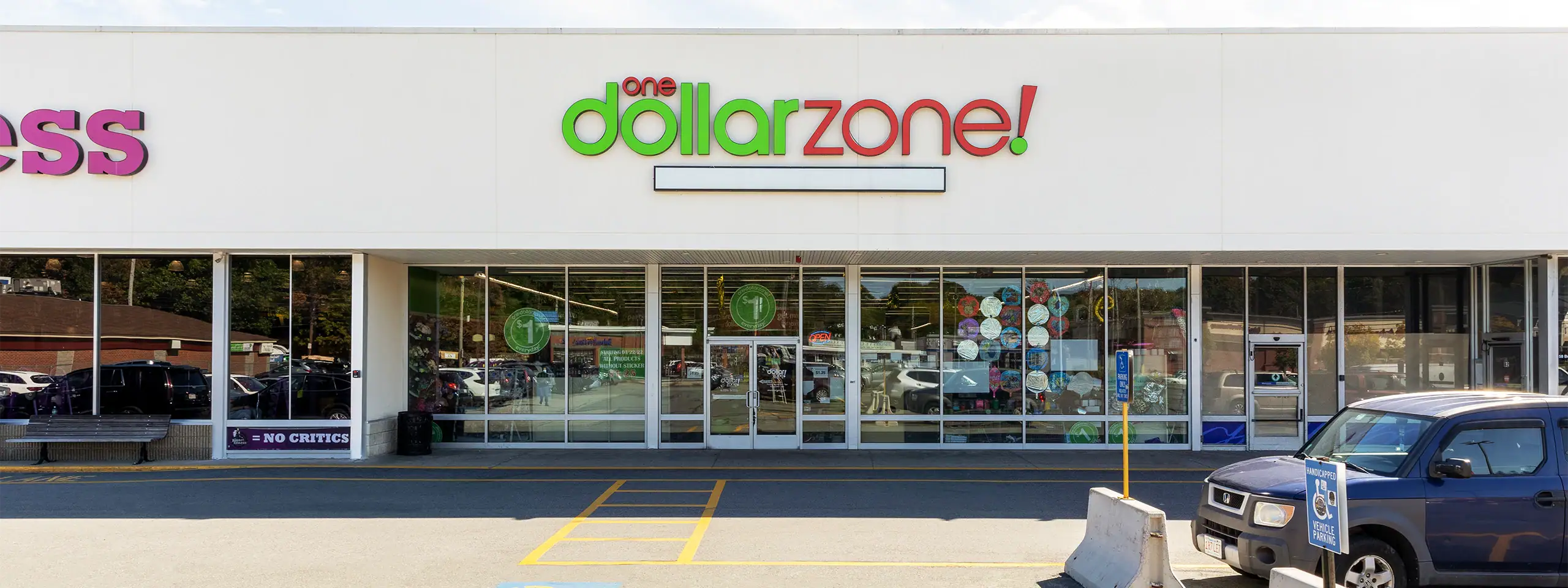 Dollar Zone store with glass storefront and parked cars outside.