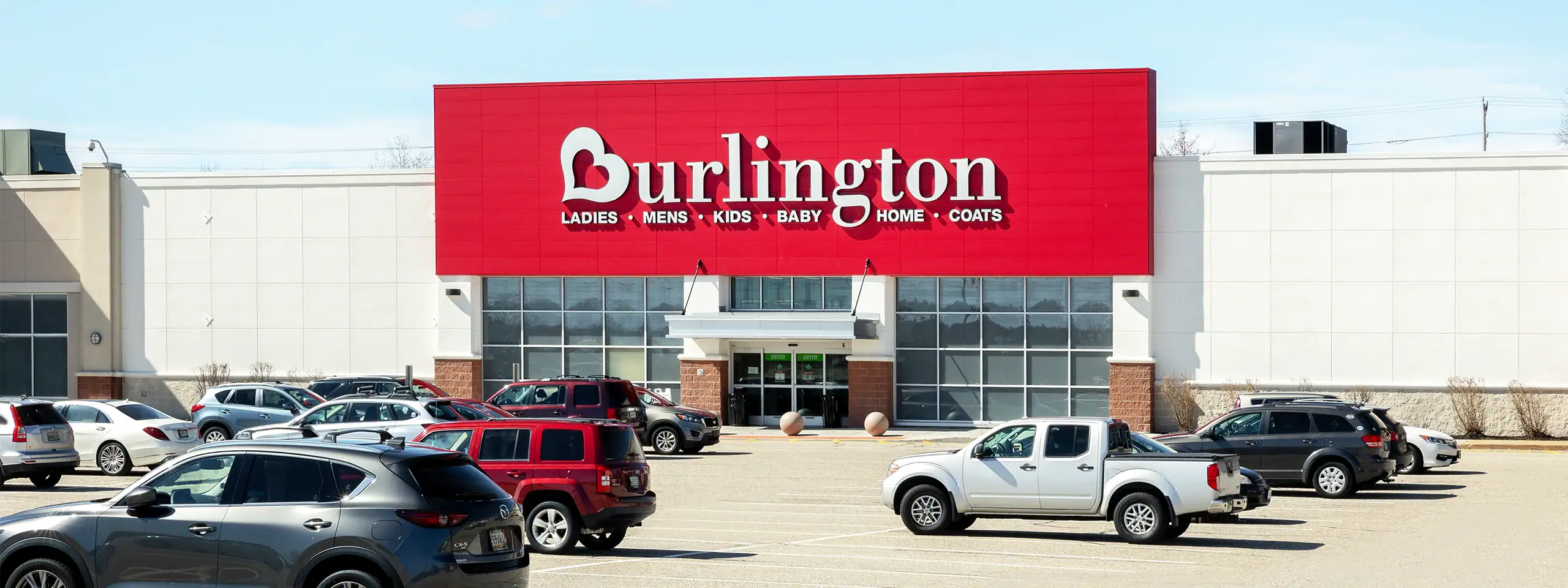 Burlington store exterior with parking lot in front, clear sky, and shopping carts.