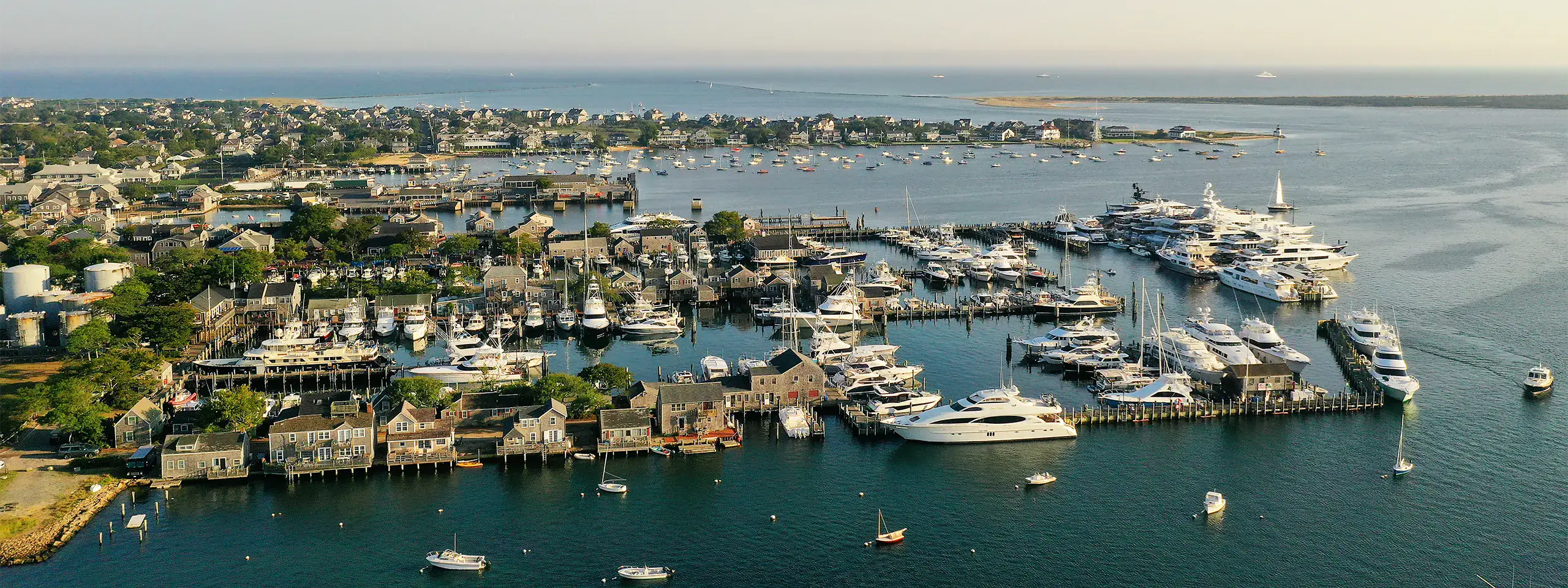 Aerial view of a marina with yachts and boats docked along a waterfront in New England.