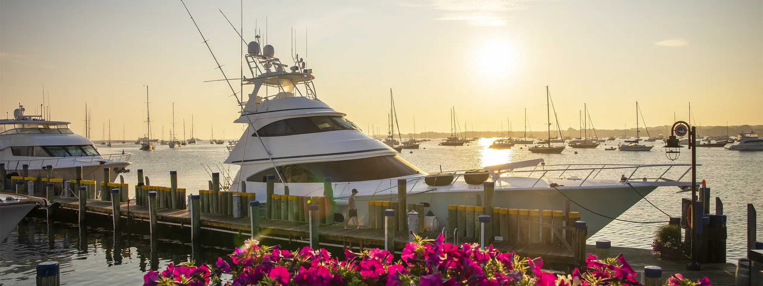 Luxury yacht docked at a marina during sunset with sailboats in background.