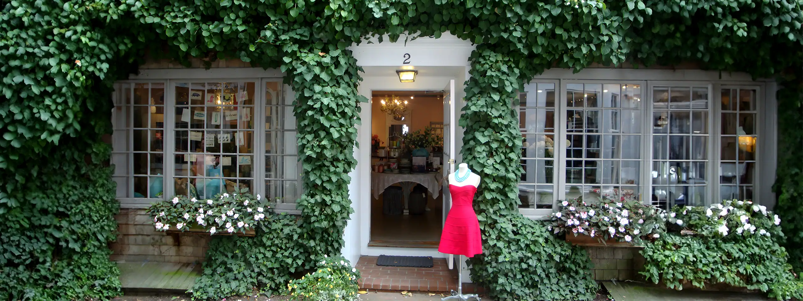 Storefront with ivy-covered walls and a pink dress on a mannequin outside.