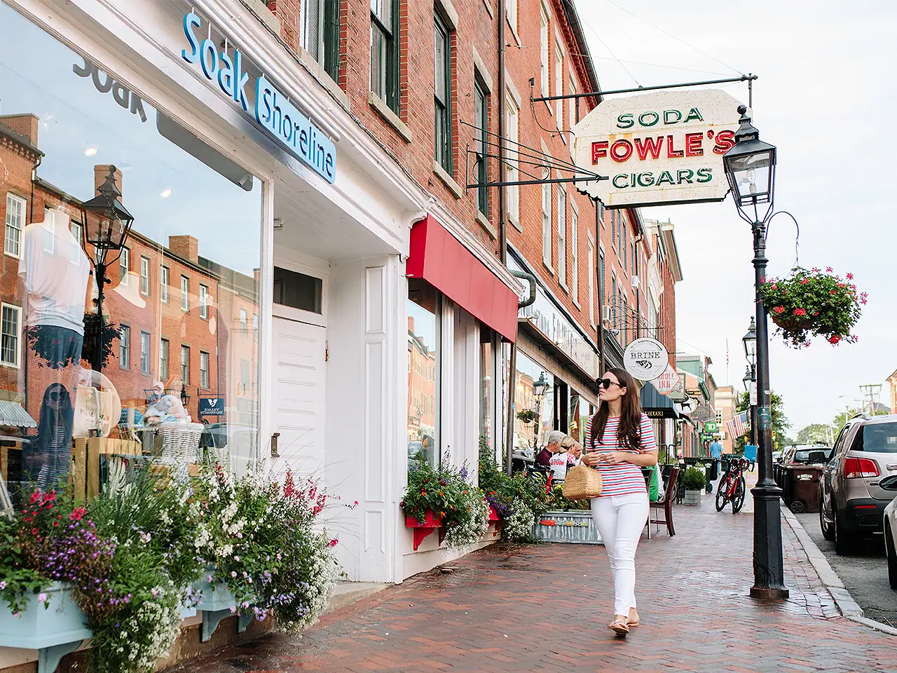 Woman walking past storefronts on a brick sidewalk in a small town.