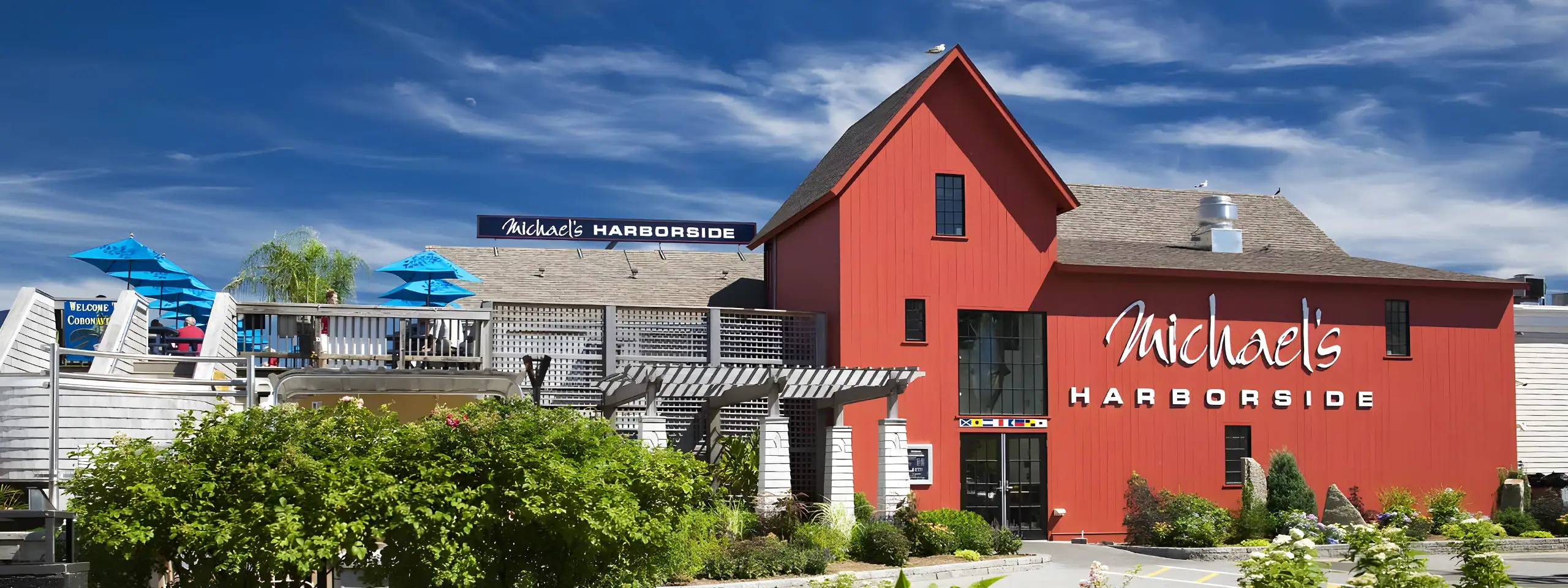 Michaels Harborside store with red building and outdoor seating area under blue umbrellas.