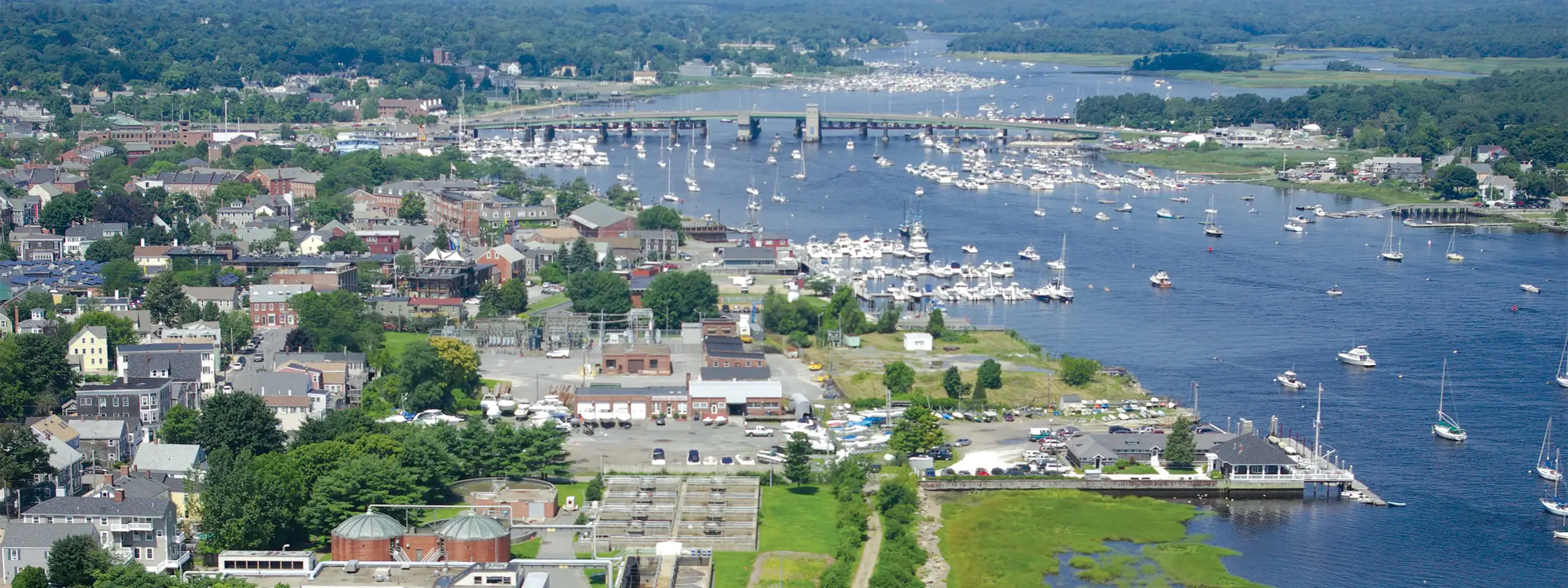 Aerial view of a harbor with boats, surrounded by a town and green landscape.