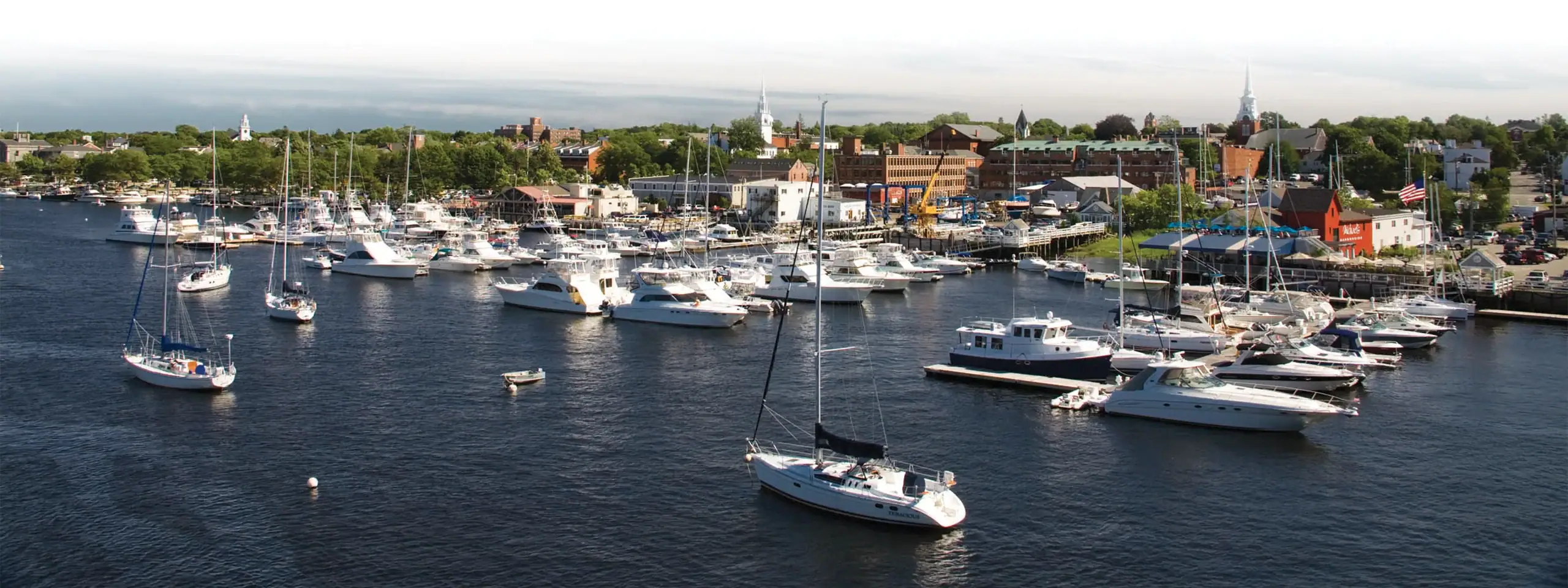 Marina with numerous sailboats and yachts docked on calm water in New England.