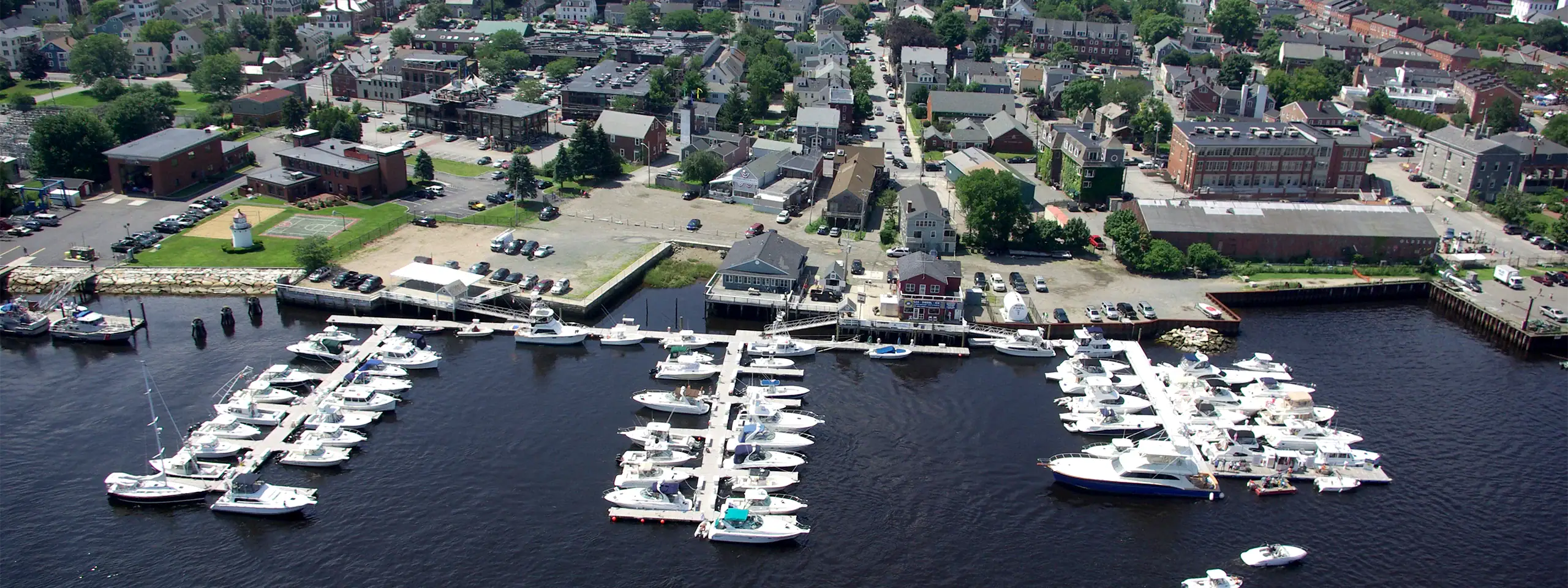 Aerial view of a marina with numerous boats docked in a harbor surrounded by buildings and greenery.