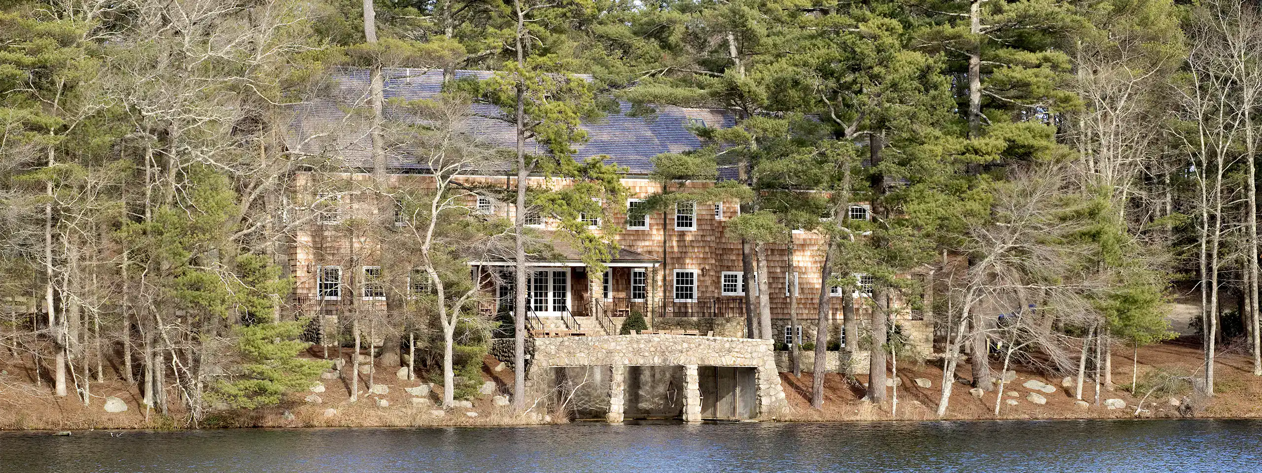 Historic brick building on a wooded lakeside with trees and water in the background.