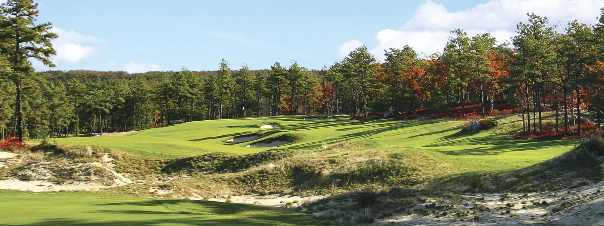 Scenic view of a golf course with lush green fairways and trees in autumn colors.