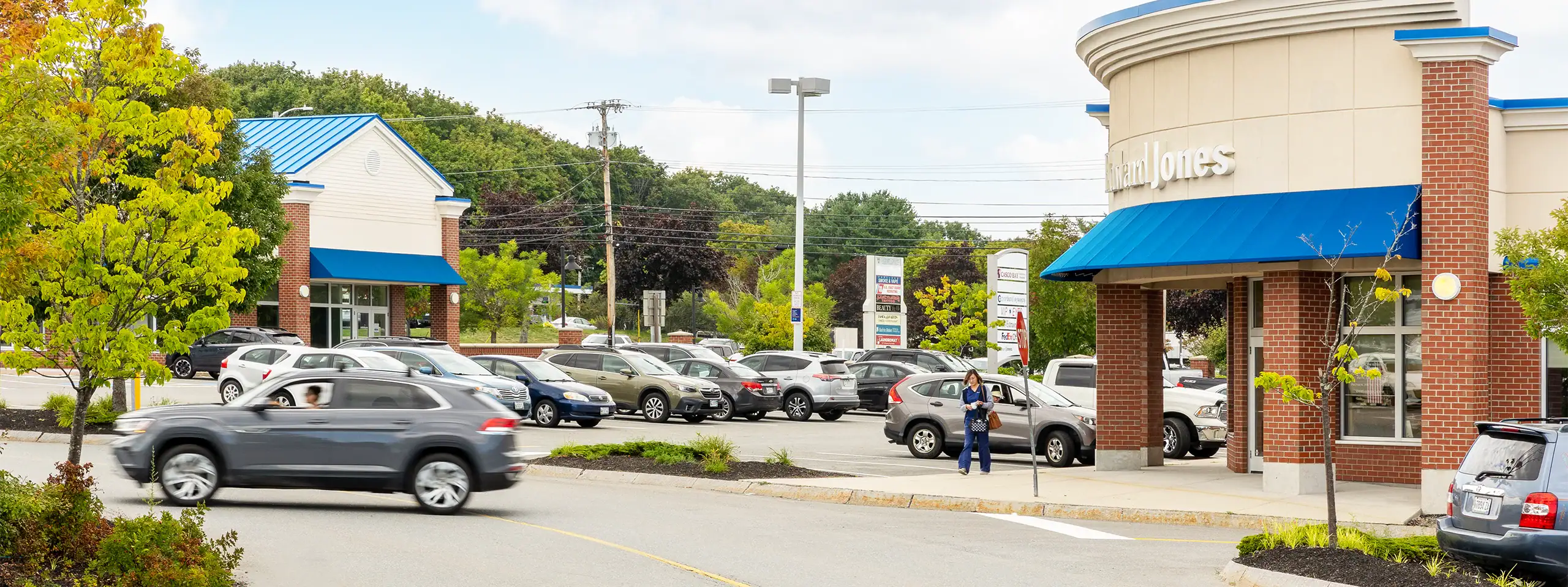 Parking lot with cars and a retail store with blue awning in New England.