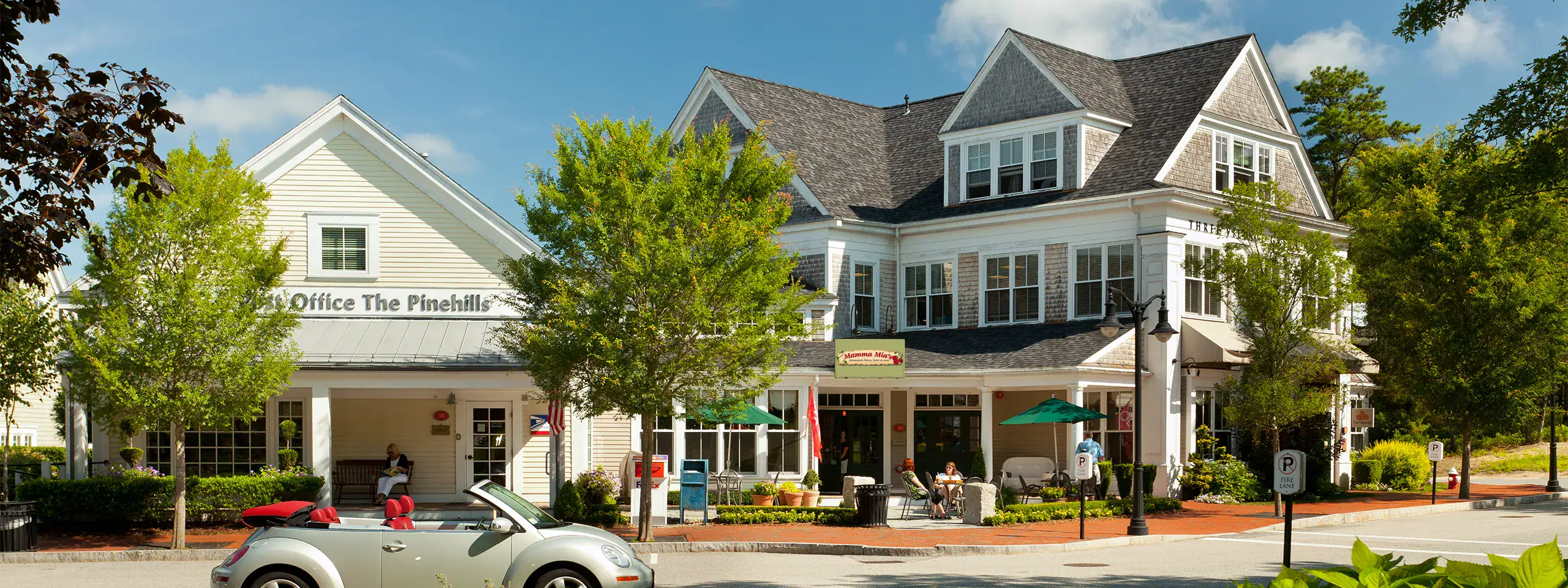 Mixed-use building with shops and offices, surrounded by trees and outdoor seating.