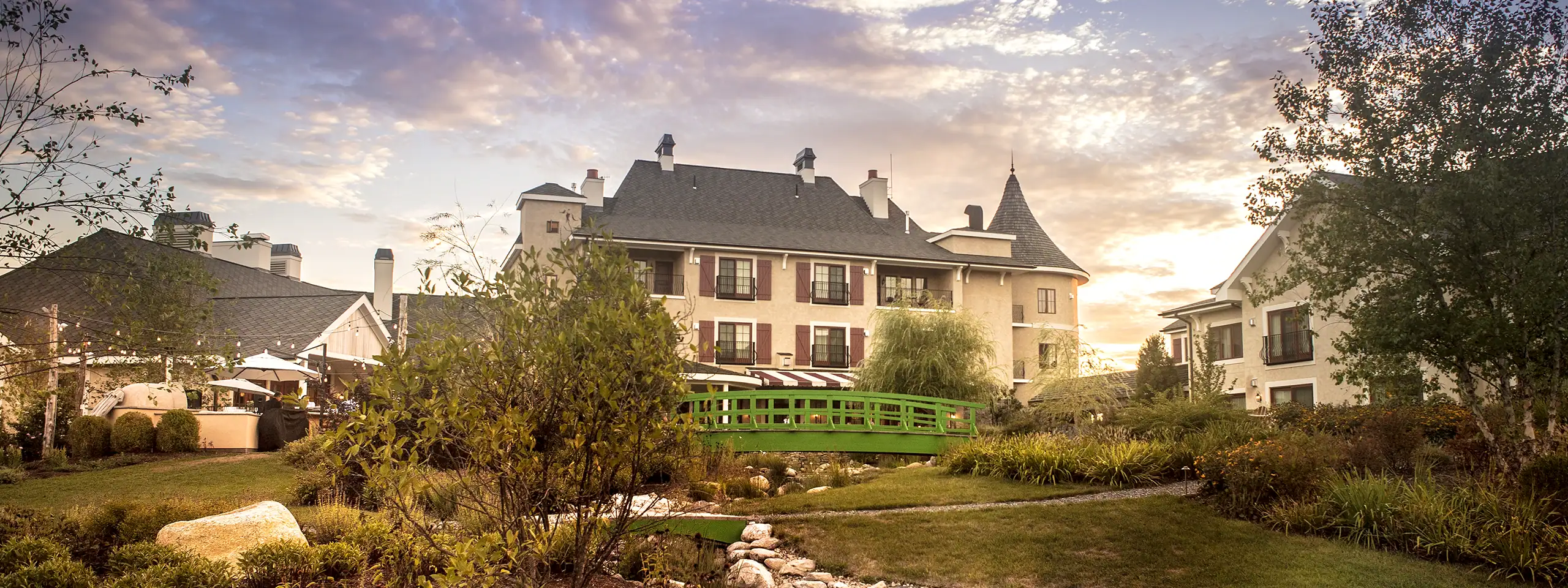 Elegant historic building with lush gardens and a green bridge at sunset.