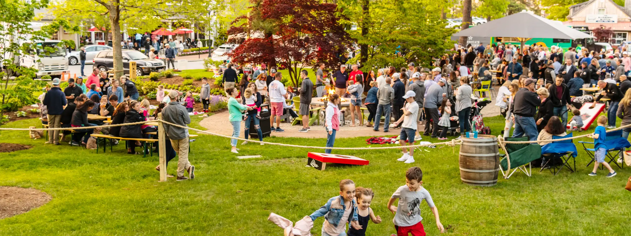Crowd gathered at outdoor event in a park with trees and tents.