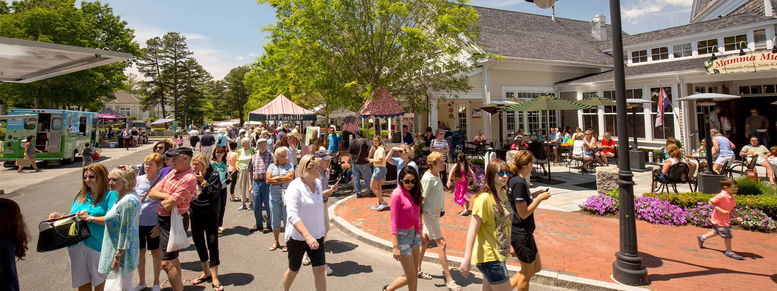 Crowd of people walking and socializing outside a shopping area in New England.