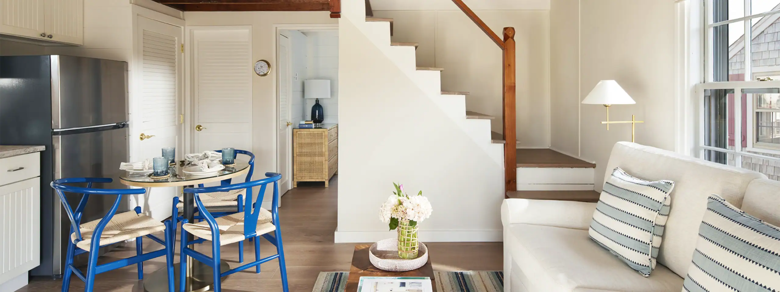 Bright living room with white walls, blue chairs, and a staircase with wooden railing.