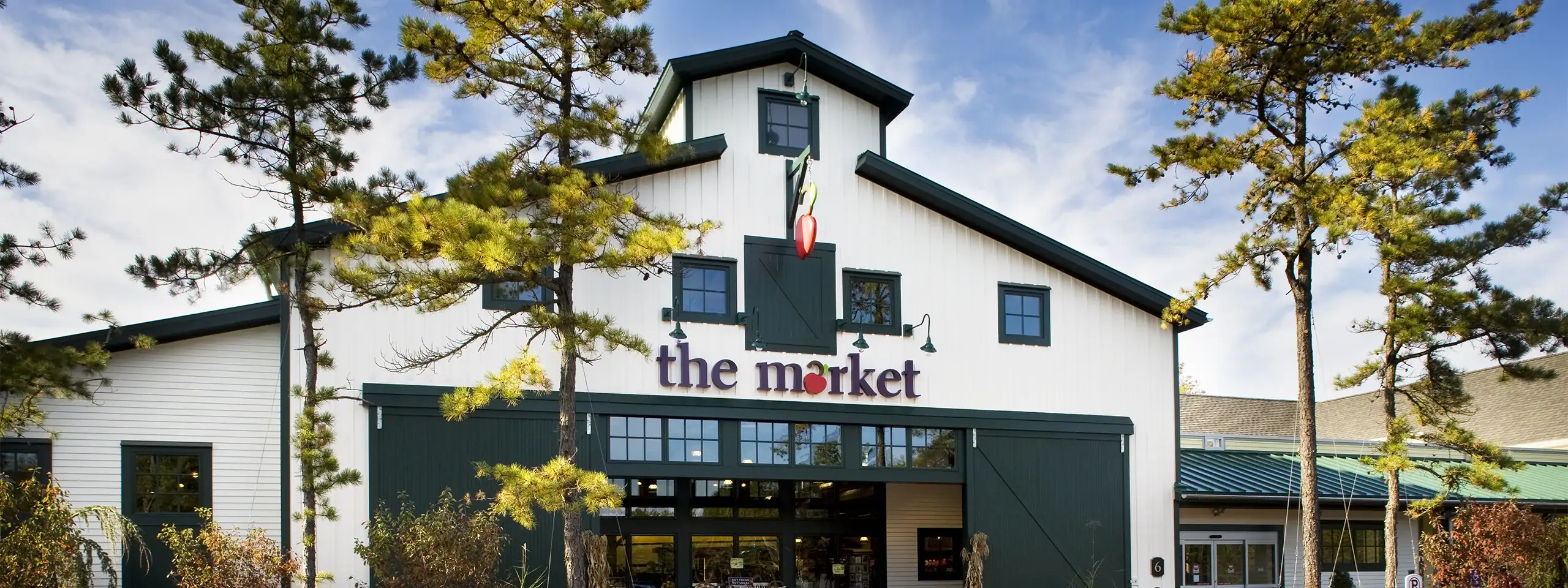 White building with green trim and a sign that says 'the market' surrounded by trees.