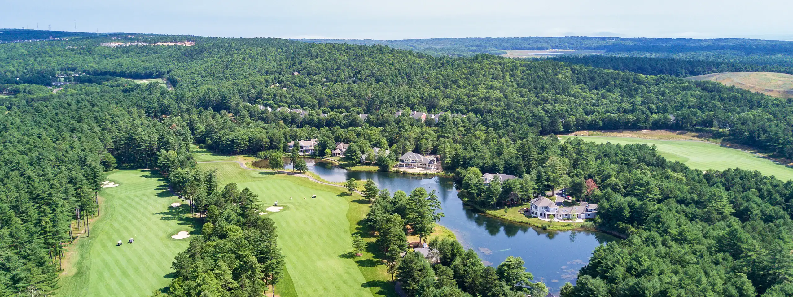 Aerial view of a lush golf course with water features and surrounding forest in New England.