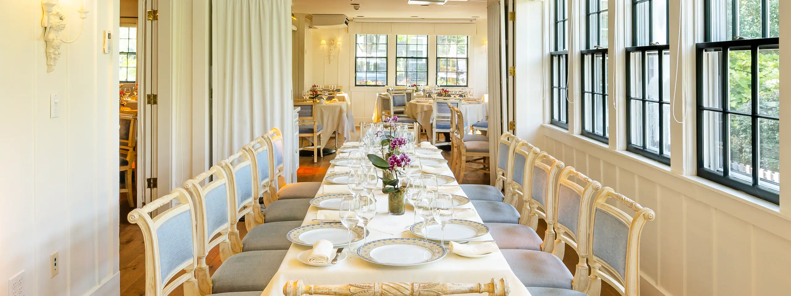 Elegant dining room with a long table set for a formal meal, bright with natural light.
