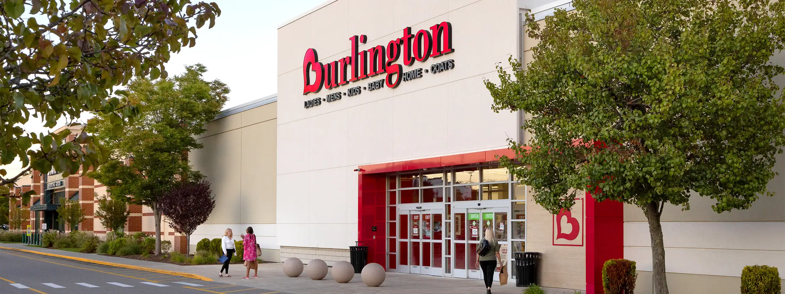 Burlington shopping mall entrance with trees and people walking outside.