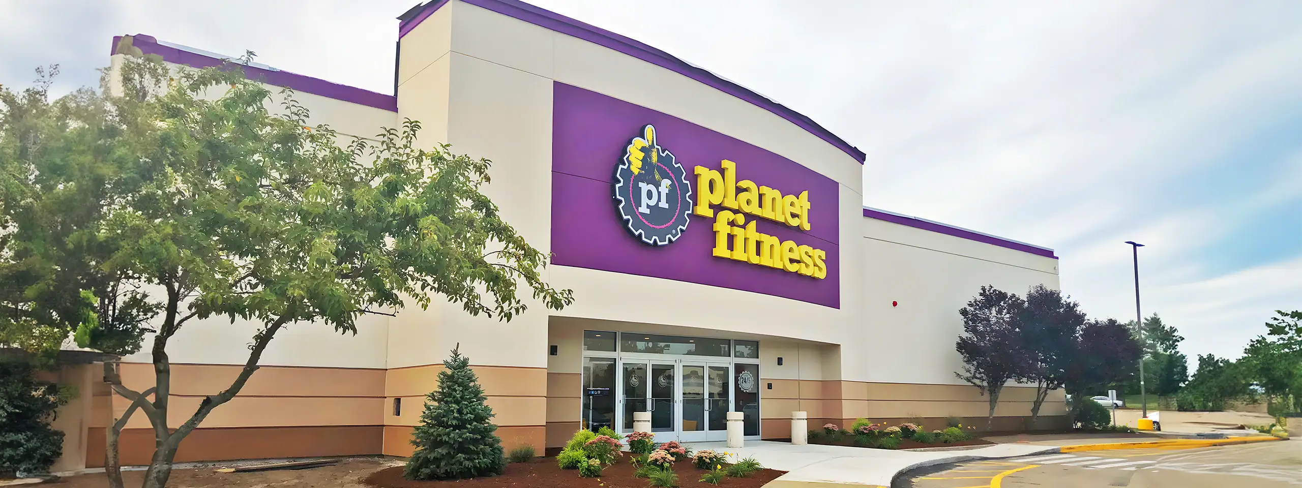 Planet Fitness gym exterior with trees and cloudy sky in the background.
