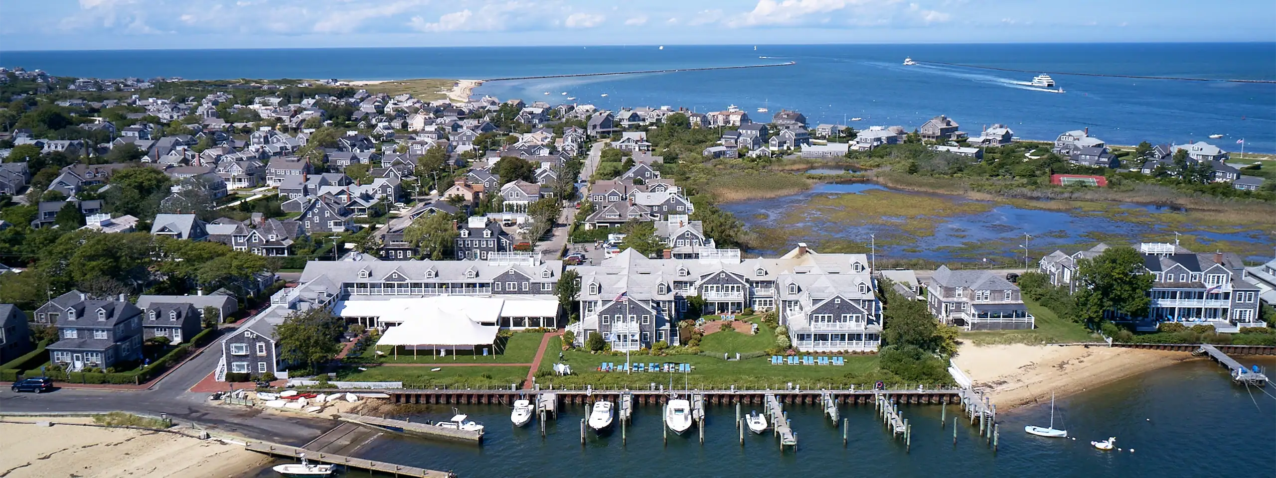 Aerial view of a coastal neighborhood with boats docked and ocean in the background.