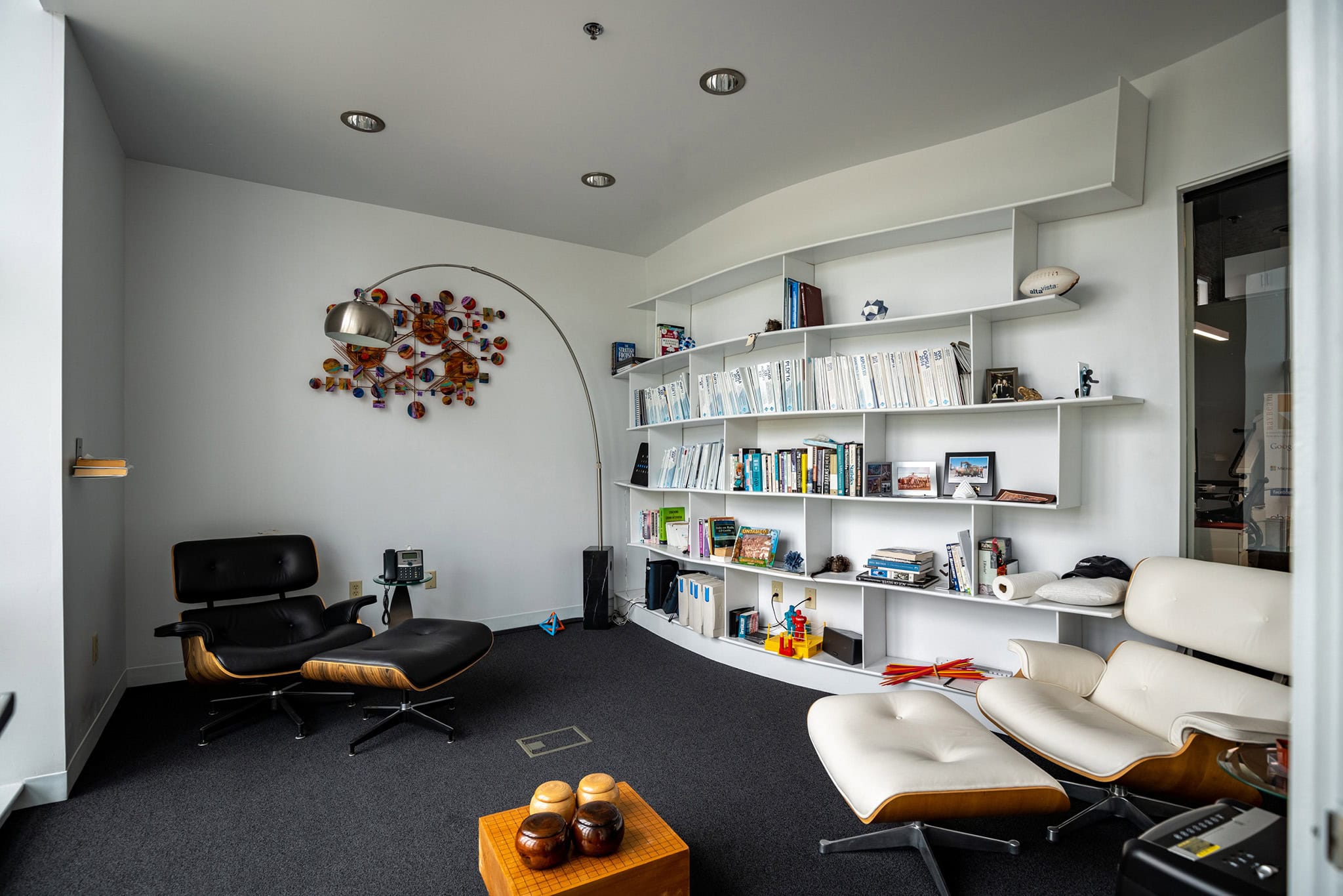 Modern office with white shelves, black and white chairs, and colorful wall art.