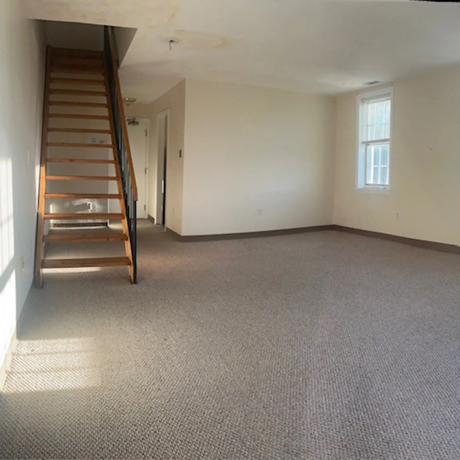 Empty living room with staircase and window in a residential space.