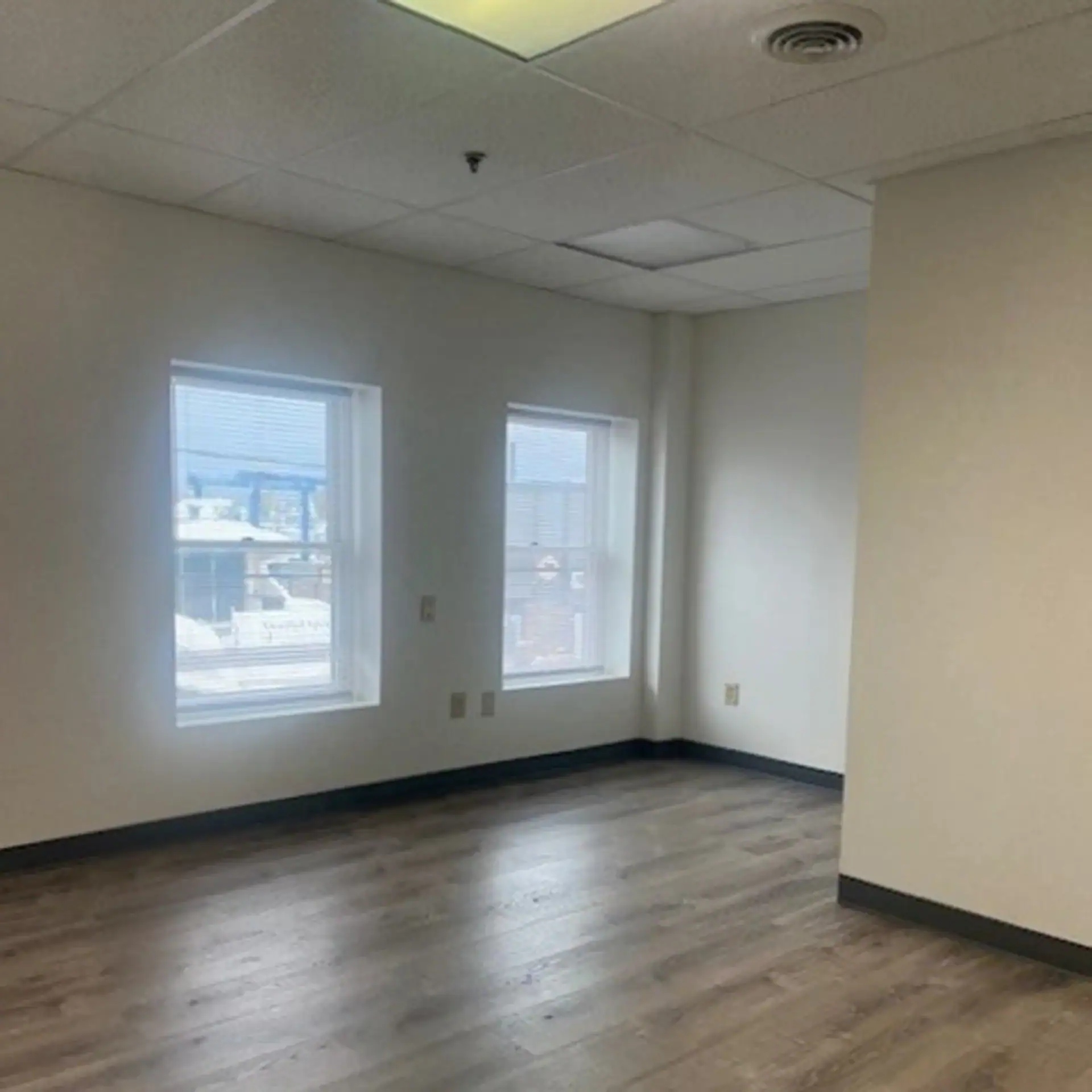 Empty room with two windows, white walls, and wood flooring in Newburyport office.