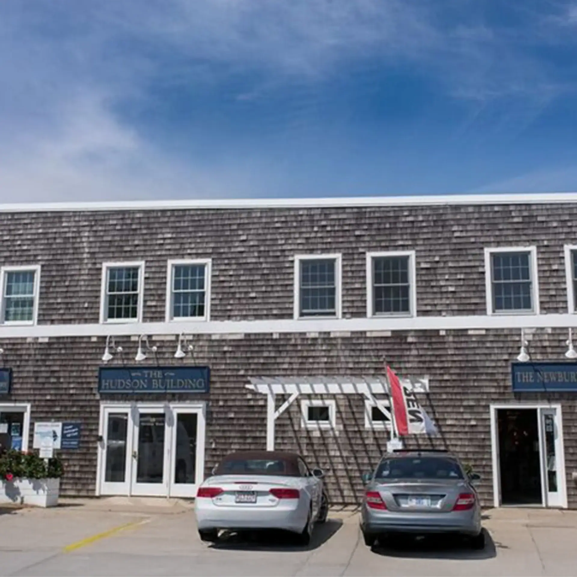 The Hudson Building in Newburyport with two parked cars in front under a blue sky.
