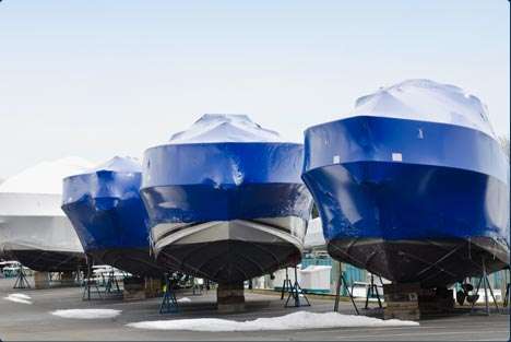 Three large boats on stands at a marina, covered with protective blue and white covers.