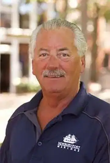 Smiling man in navy polo shirt with 'Marina' logo outdoors.