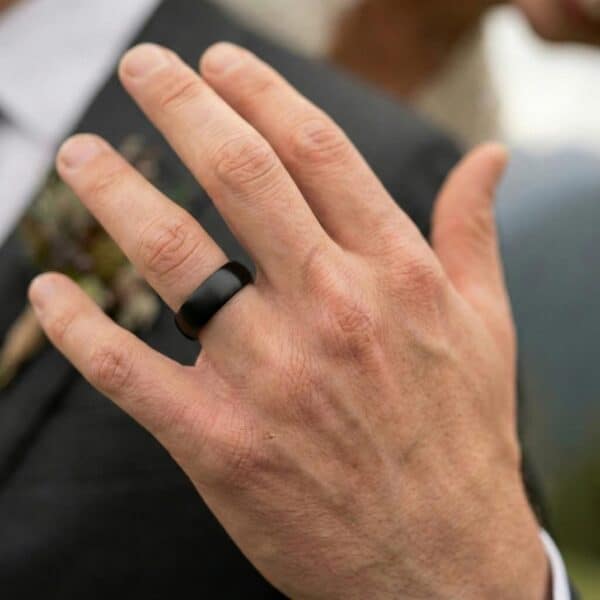 A close up of a mans hand wearing his brand new wedding ring. It is a black tungsten band with blue on the interior.