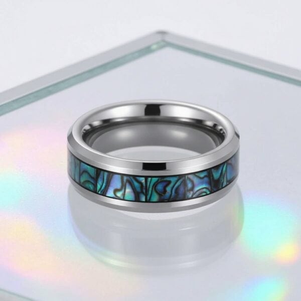 Set on an iridescent glass tray, the image focuses on a ring. It is a silver tungsten ring with an abalone shell inlay.