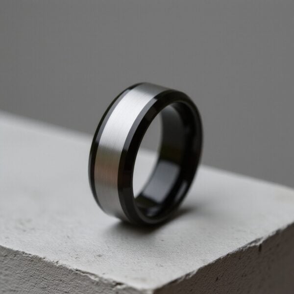 On a concrete block, a silver and black ring stands upright. The centre of the ring is brushed silver and the edges are polished black.