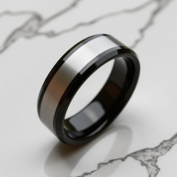 Standing upright on white marble is a silver and black tungsten ring. The inside of the ring is polished black.