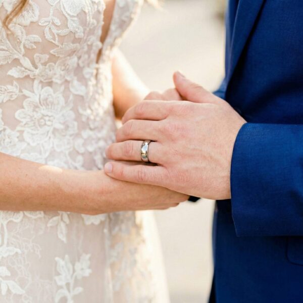 During the wedding ceremony, the newly married couple join hands. The man is wearing his new wedding band which is a polished silver tungsten ring. It is slightly domed in shape and is the style of a classic mens wedding ring.