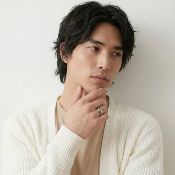 Looking away from the camera to one side, the man holds his hand to his chin in a thoughtful pose. He wears a polished silver tungsten ring on his finger.