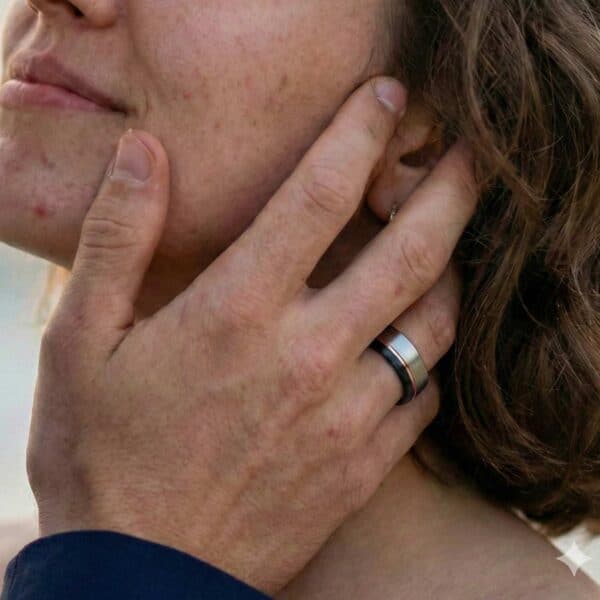 Cupping his partners face with his hands, the woman looks up towards him. On his hand, the man has a tungsten ring that is made up of a selection of colours - silver, rose gold, and black.