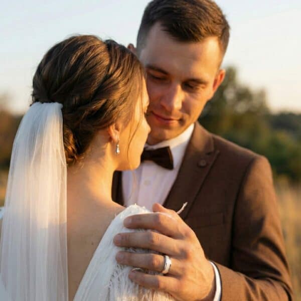 With an idyllic countryside scene in the background, a newly married couple face on another. The man puts his hand on the woman's shoulder. On his hand, he is wearing a silver tungsten ring. It has an inlay of mother of pearl.