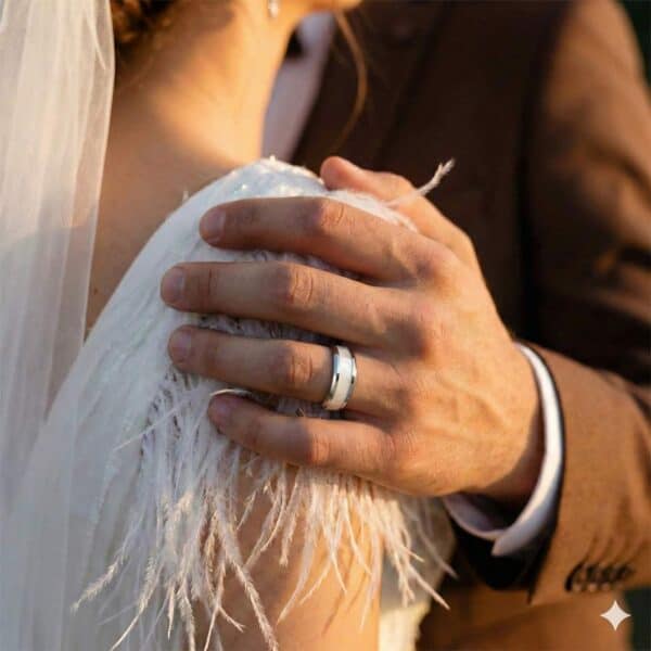 The wedding couple stand together, the man with his hand on the womans arm. He wears a silver tungsten ring that has an inlay of mother of pearl.