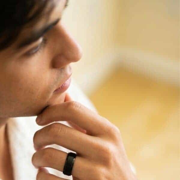 You can see the profile of a mans face. He has his chin resting on his hand. On his hand, he has a black tungsten ring shown in close up. The ring has a raised centre which has a brushed finish and stepped edges that are polished.