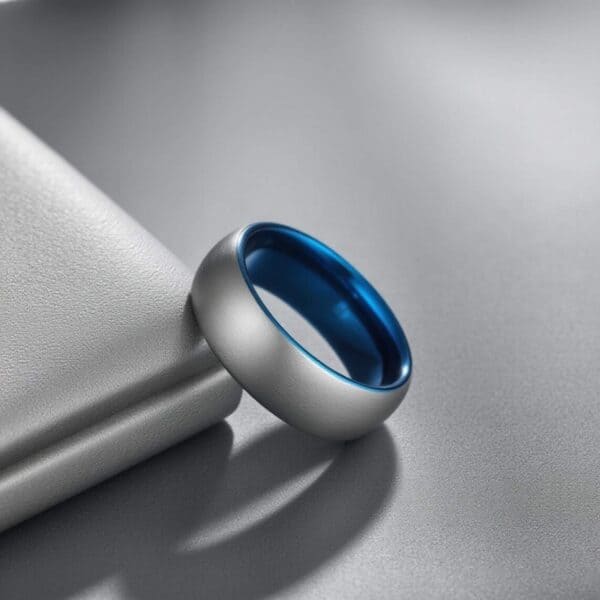 Learning against the side of a silver tablet, the image focused on a silver ring. The ring is made with tungsten and has a lightly brushed finish. The inside of the ring is polished blue.