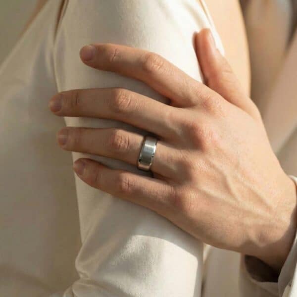 The man reaches out to hold his partners arm. On his hand he wears a silver tungsten ring. It has a brushed silver centre section and polished bevelled edges. The inside of the ring is vibrant red.