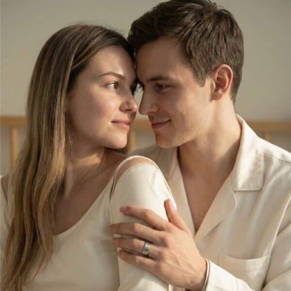 A couple embrace and gaze into each other's eyes. The man wears his new wedding band - a silver tungsten ring with a mix of brushed and polished finishes. The inside of the ring is bright red.