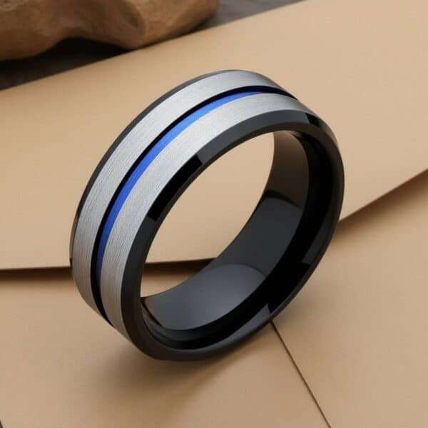 A close up image of a silver tungsten ring featuring a blue groove and polished black edges. The ring is upright, on top of a brown envelope.